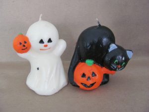 A pair of candles, one a ghost holding a pumpkin, the other a black cat with green eyes holding a pumpkin.