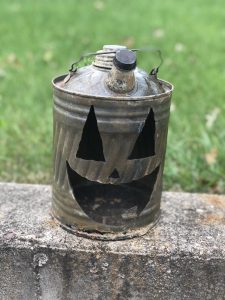 This faux pumpkin is a hollow jack-o-lantern face carved into a vintage, metal, dome gas can.