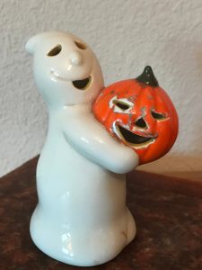 A small, white, smiling ceramic ghost holding a smiling jack-o-lantern.