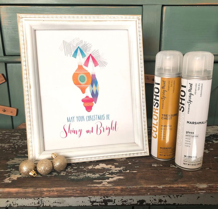 A white and gold frame showcases a holiday art printable with Shiny Brite ornaments. COLORSHOT spray paint is the product.