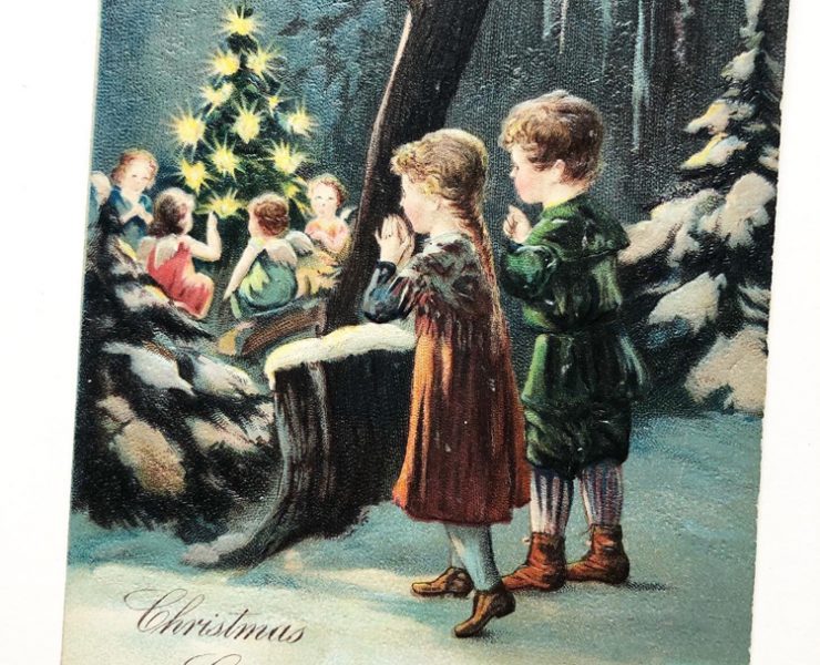 Postcard with two children in the snowy woods watching angels around a tree.