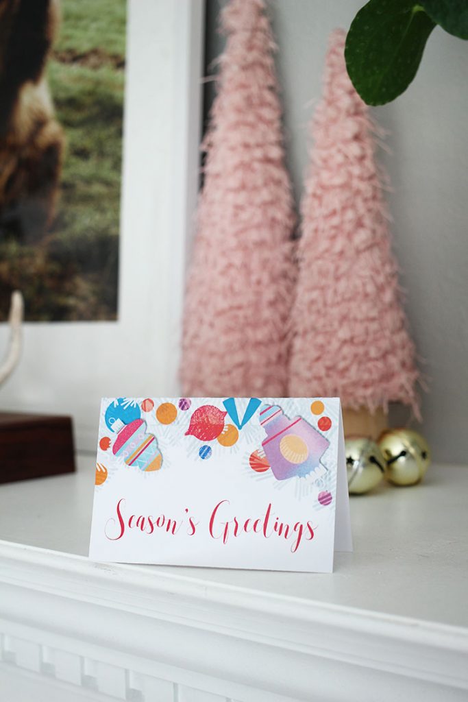 A Season's Greeting holiday card sits in front of pink Christmas trees with jingle bells.