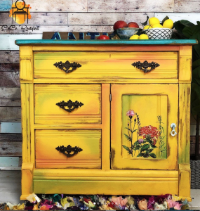 Bright yellow dresser with a teal top and floral design on one cupboard door.