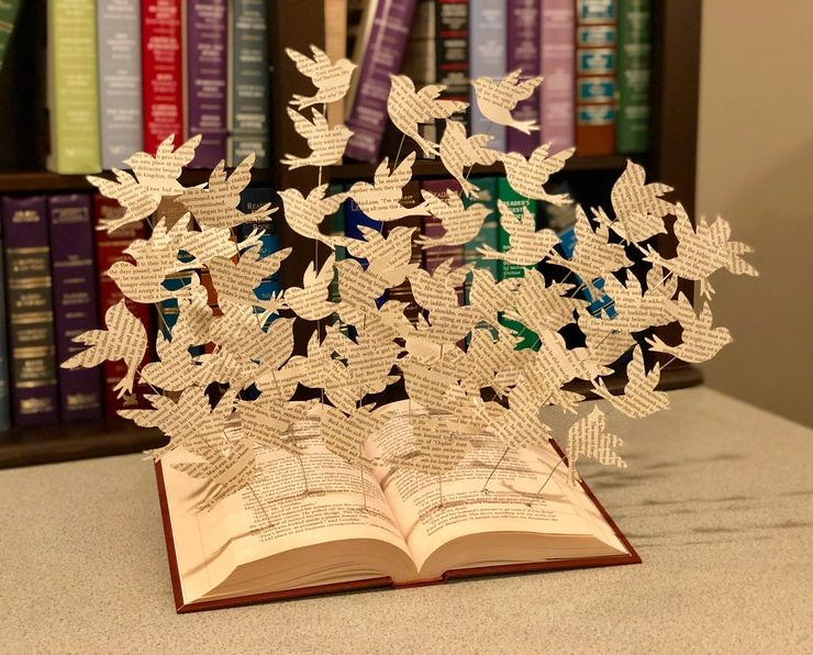 Open book with cut out birds flying out of it.
