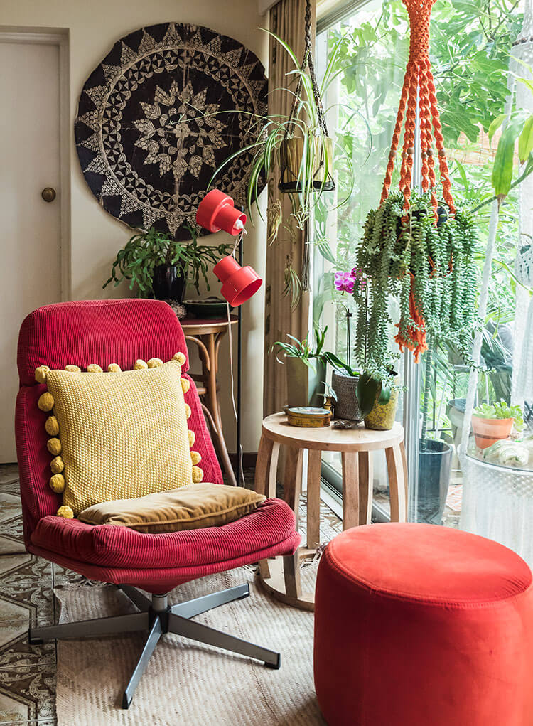 The interior of a vintage-inspired home featuring a chair with a red facade, hanging plant, and an intricate tapestry that all steal the show.