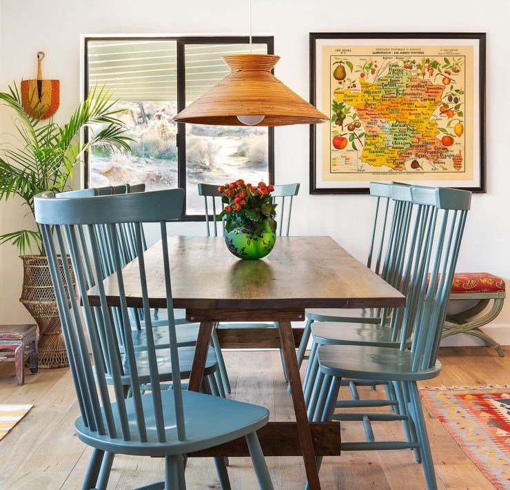 A moroccan home renovation highlighting the dining room's woven fans and blue chairs that complement a sleek wooden tabletop.
