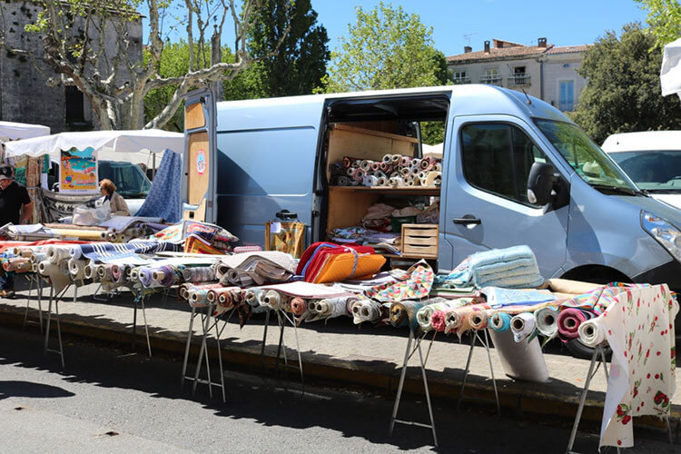 A truck at a Provence market loaded with multi-colored rugs.
