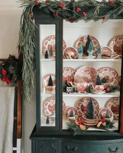 dark green hutch with vintage red and white china decorated for Christmas with bottlebrush trees