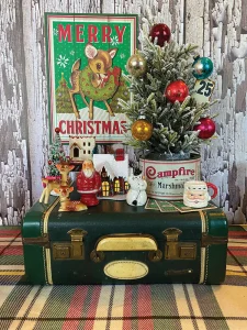 vintage suitcase serves as the base for a Christmas vignette with vintage tins, Santa and snowy house