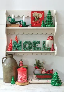 red and green holiday vignette on decorative shelving unit featuring holiday candles