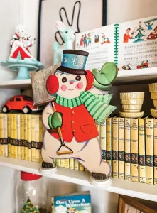 snowman cutout and vintage Christmas sheet music on display in front of bookshelf