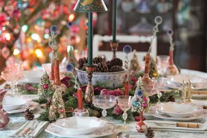 holiday tablescape decorated with blue thistle in bud vases and mini trees around centerpiece with bowl of pinecones