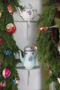 Old World pitchers on corner shelves surrounded by holiday garland with vintage ornaments